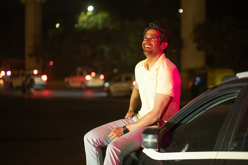Smiling young man sitting on car hood at night