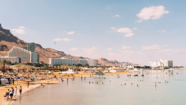 Ein Gedi Beach Dead Sea Israel Coastal Panorama Crowded Ein Gedi Beach Israel Dead Sea Coast Panorama. View along the Dead Sea coastal Ein Gedi Beach with Travellers and Tourists swimming enjoying the bath in the salty, mineral Dead Sea Waters. Turquoise salt water of the Dead Sea under summer skyscape. Dead Sea, Ein Gedi Beach, Israel, Middle East. desert wash stock pictures, royalty-free photos & images