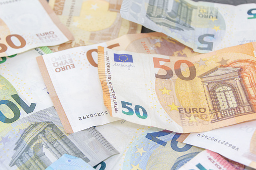 A close-up photo of various euro bills including 5, 10, 20, 50, and 100 denominations spread out on a table. Financial concept.