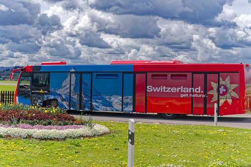 Red and blue tour bus with tourist advertising parked at Swiss Airport Zürich Kloten on a blue cloudy spring day. Photo taken April 14th, 2023, Kloten, Canton Zurich, Switzerland.