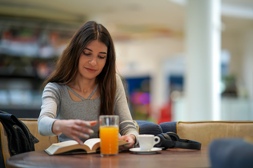 Young woman drinking juice and reading a book in the neighborhood cafe.