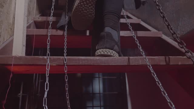 the legs of the prisoner in chains closeup. feet step upstairs. red light. abandoned house. high quality FullHD footage with slow motion.