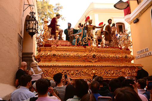 Cordoba-Spain/ 3-April 2023: Samana Santa From the church is comming out a gilded parade float with on top figurines.Crowd of people looking at it. Rear view.