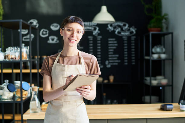 istock Young brunette female clerk of cafeteria making notes in notepad 1484742220