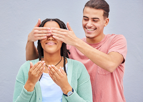 Wow, surprise or hands and a couple on a gray background outdoor with a man covering the eyes of his girlfriend. Diversity, hands or dating with a woman being surprised by her boyfriend on a wall