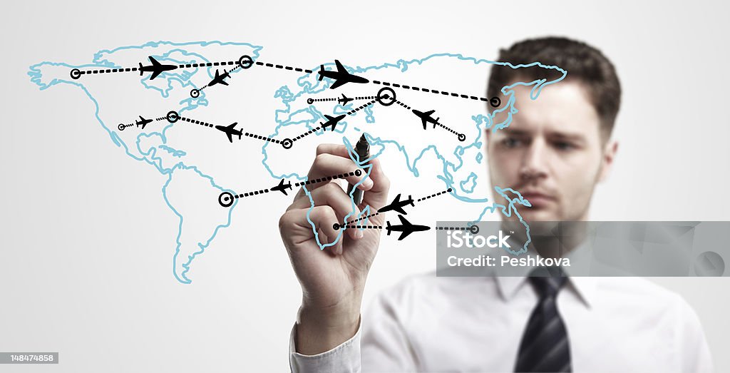 Young business man drawing an airplane routes on world map Young business man drawing an airplane routes on world map. Man drawing world map with aircraft flying on a glass window. The metaphor of international air travel around the world Adult Stock Photo