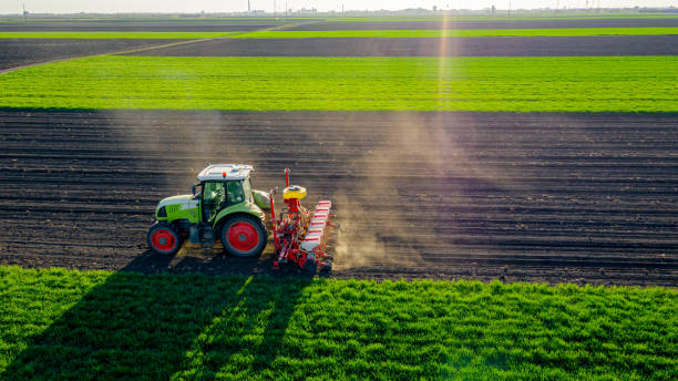 vista aérea del tractor arrastrando una máquina de siembra sobre el campo agrícola, las tierras de cultivo - tractor green farm corn fotografías e imágenes de stock
