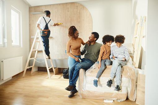 Happy black family moving into a new home while manual worker is in the background.
