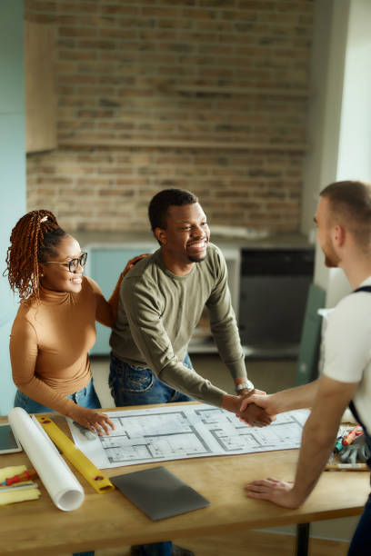 istock Happy black couple shaking hands with manual worker in moving house. 1484754638