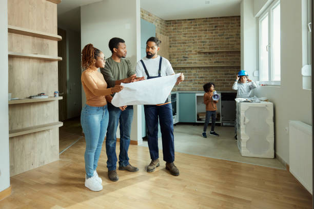 Black parents and manual worker analyzing blueprints in the apartment.