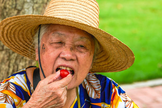 cheerful senior woman in garden holding apple, table with mixed vegetables in background