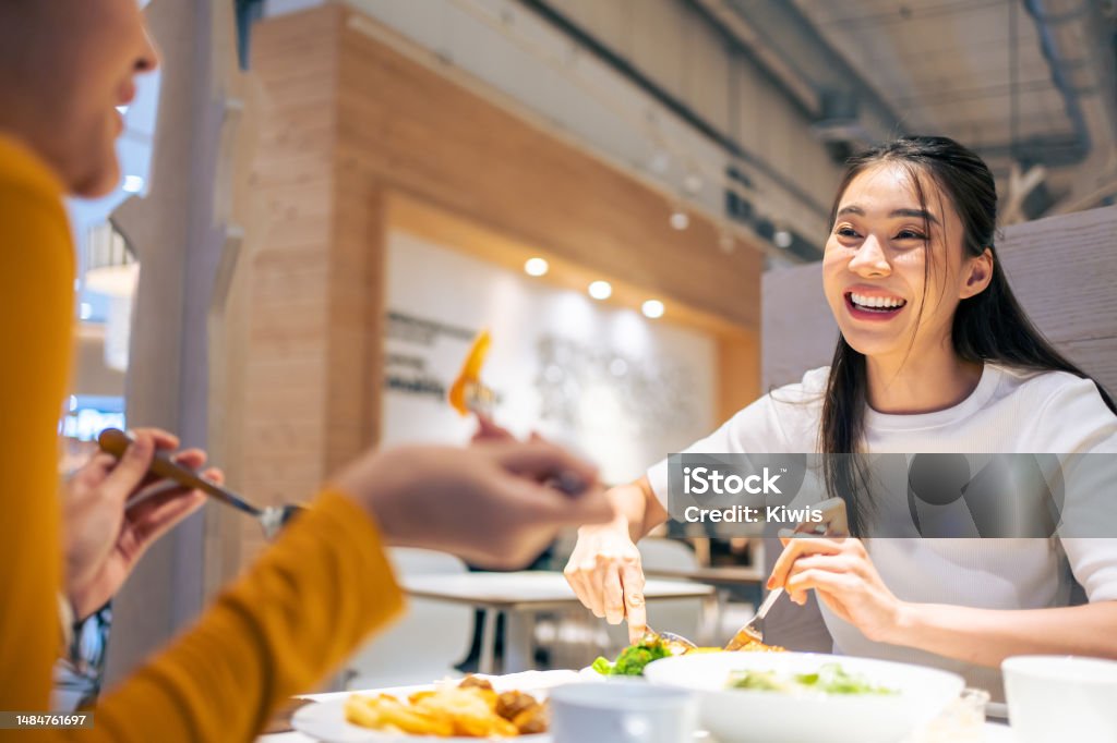 Asian beautiful women having dinner with friend in restaurant together. Attractive young girl feeling happy and relax, having fun talking and eating food at their table in dining room in cafeteria. Dining Stock Photo