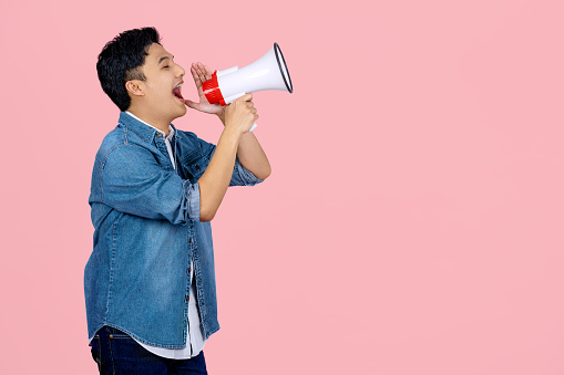 Handsome Asian young man speaking using megaphone to sideways. Isolated on white