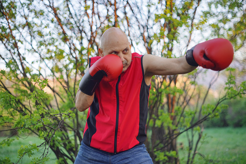 A middle-aged man in boxing gloves does a light workout in the fresh air.