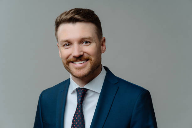 Happy successful entrepreneur in suit smiling at camera while posing against grey background