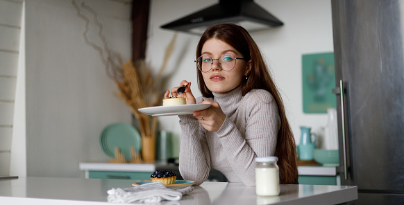 Young attractive woman in home interior eating sweets in a relaxed way in the kitchen.