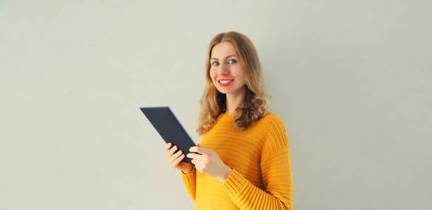 Portrait of happy smiling young caucasian woman with tablet pc or e-book on gray background stock photo