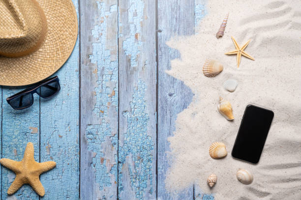 istock Summer, beach and vacation concept with free text space. Top view. Flat layout with a man straw hat, sun glasses, smartphone, various sea shells and fine beach sand on an old blue wooden boards background 1484771286