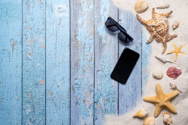 istock Summer, beach and vacation concept with free text space. Top view. Flat layout with a smartphone, sun glasses, large sea star and sea shell and various sea shells and fine beach sand on an old blue wooden boards background 1484771901