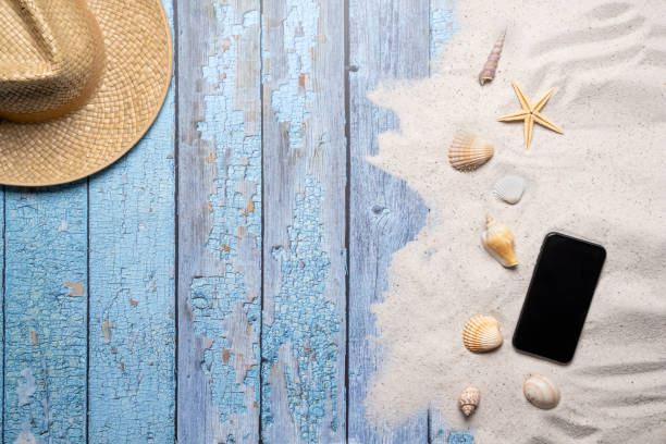 istock Summer, beach and vacation concept with free text space. Top view. Flat layout with a man straw hat, smartphone, various sea shells and fine beach sand on an old blue wooden boards background 1484772029