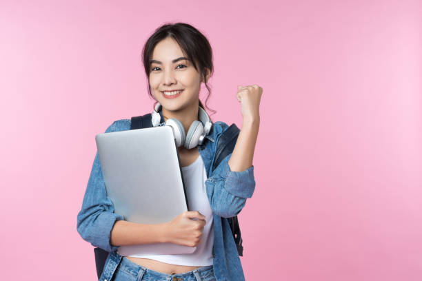 retrato de un joven estudiante universitario asiático sonriente con computadora portátil y mochila aisladas sobre fondo rosa. animar el concepto de celebración del éxito - filipino ethnicity audio fotografías e imágenes de stock