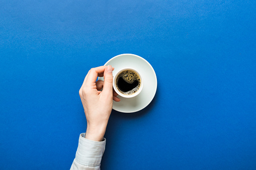 Minimalistic style woman hand holding a cup of coffee on Colored background. Flat lay, top view cappuccino cup. Empty place for text, copy space. Coffee addiction. Top view, flat lay.