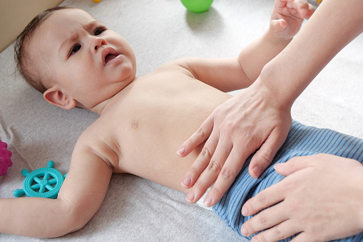 Masseur massaging the tummy of the baby during colic. Mother massaging infant belly, kid laughing.
