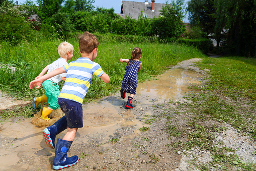 Three children, two boys and a girl, running through puddles in rubber shoes.