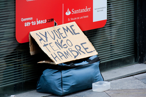 Madrid, Spain_ June 18, 2012: Help me, I am hungry, handwritten sign on sidewalk in front of bank office. Madrid, Spain. Small plastic box for alms.