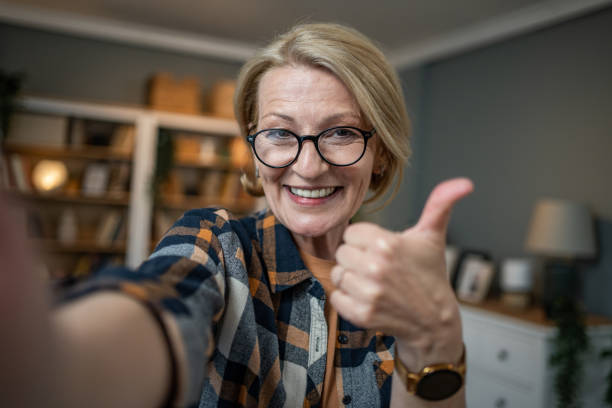 Caucasian mature woman taking selfie or video call using mobile phone or vlog camera having happy facial expressions