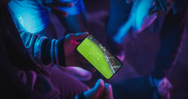 istock Close Up Smartphone Screen with a Soccer Championship Live Broadcast. Group of People Using the Mobile Phone, Following a Sports Internet Stream, Supporting Their Football Team 1484786635