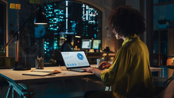 istock Creative Multiethnic Female Working on Laptop Computer with a Sales Statistics and Chart Displayed on Screen. Successful Designer Developing a Marketing Strategy, Preparing a Presentation 1484786775