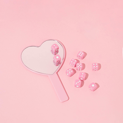Valentines day creative layout heart shaped mirror and pink dices on  pastel pink background. 80s, 90s retro romantic aesthetic love concept. Minimal fashion cosmetic idea.