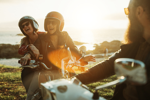A group of friends enjoy the warm sunset with a trip on motorbike. Two women and a man group