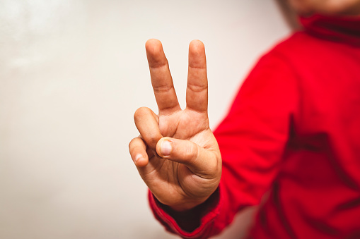 gesture and people concept - portrait of little boy in red hoodie showing peace hand sign over grey background - V sign