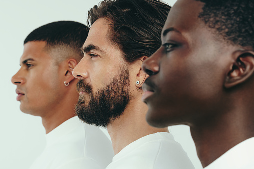Three men standing in a studio, confident and proud of their flawless, glowing skin. Men with diverse skin tones showing off their natural beauty and the results of a consistent skincare routine.
