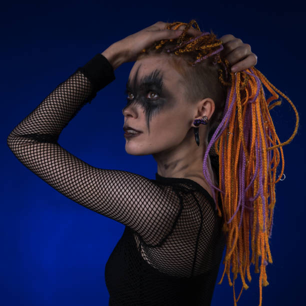 Dramatic portrait of young female with spooky black stage makeup painted on face and orange color dreadlocks hairstyle stock photo