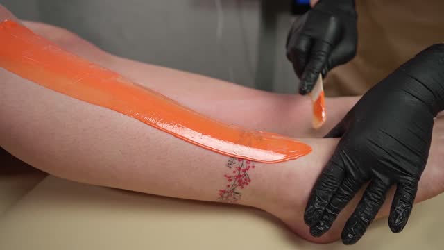 A master applies Depilatory Wax to a young woman's leg for Hair Removal. Depilation with wax. Close-up