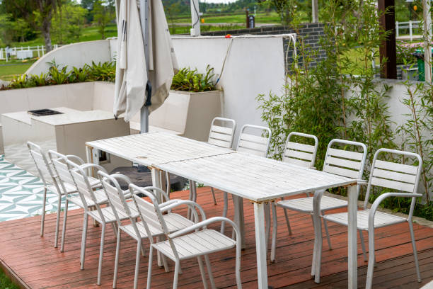 A beautifully arranged wooden patio table set for lunch outdoors, surrounded by lush green trees. Features white plates, glassware, wine bottles, and sunlight filtering through the leaves.
