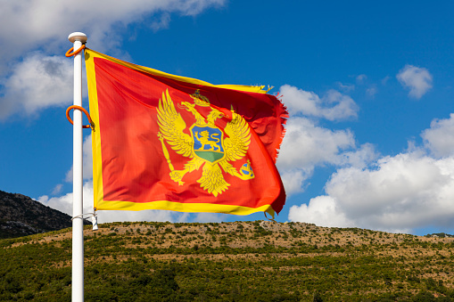 Flag of Montenegro waving in the wind with sky and mountains in background