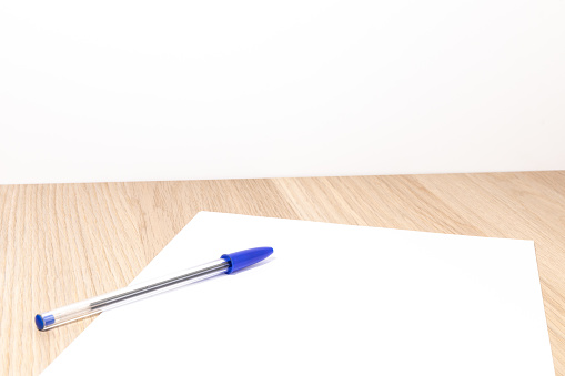 Blank sheet of paper and pen on bright wooden office desk.