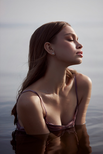 Beautiful romantic young woman is resting on the lake. Perfect body, a woman in the water at sunset