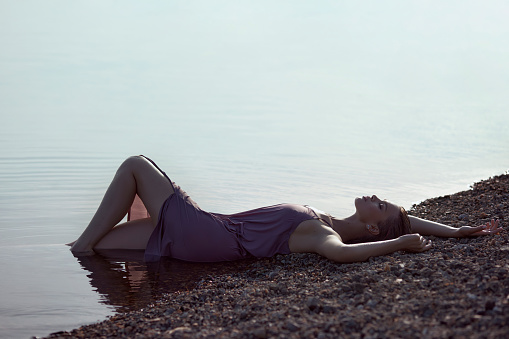 Beautiful romantic young woman is resting on the lake. Perfect body, a woman in the water at sunset