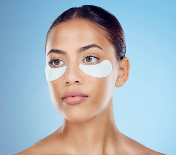 Black woman with collagen eyes mask isolated on blue background for skincare, beauty and facial cosmetics. Young model or person with dermatology eye patch, anti aging product and skin glow in studio mujer negra con ojos de colágeno máscara aislada sobre fondo azul para el cuidado de la piel, belleza y cosmética facial. modelo joven o persona con parche ocular dermatológico, producto antienvejecimiento y brillo de la piel en el estudio