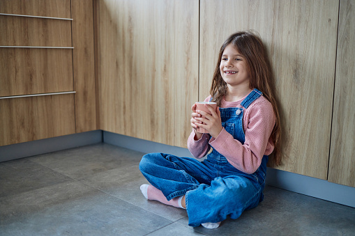 Portrait of a beautiful girl sitting in the kitchen floor, relaxing. She is holding cup.