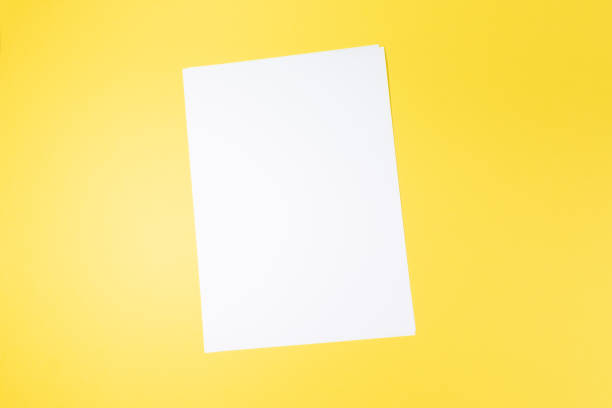 istock empty white paper sheet and on yellow background. Mockup 1484800880