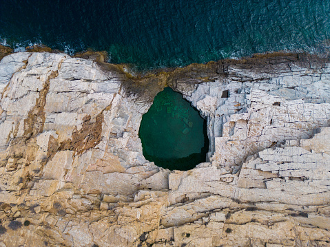 top down aerial view of Giola on the Greek island of Thassos is a breathtaking sight to behold. The natural swimming pool's crystal-clear turquoise waters, surrounded by rocky cliffs and lush greenery, create a mesmerizing visual spectacle.