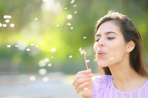 Happy woman blowing dandelion in spring