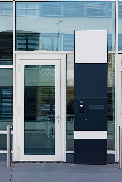 corporate entrance glass door and a black metal stele with doorbell, intercom and mailbox has white spaces where logos could be pasted in. architectural stele stock pictures, royalty-free photos & images