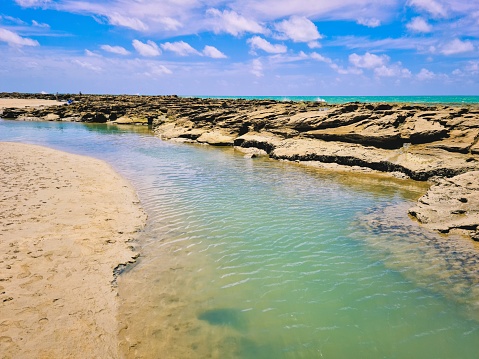 Low tide making natural pools at Forte beach, and urban beach in Natal, Rio Grande do Norte, Brazil. Colorful sky and clear sea water. Sunny day at the beach.